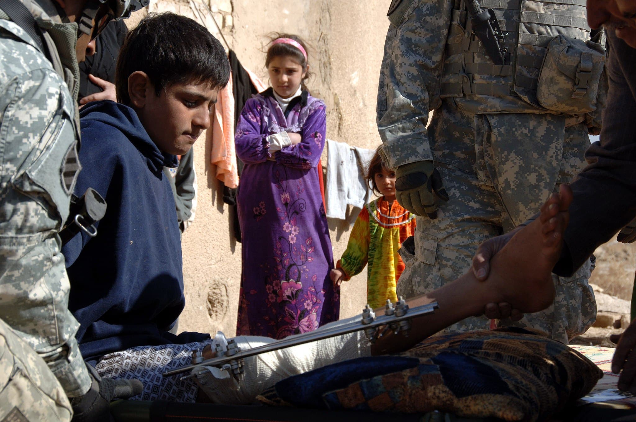 Un soldato statunitense sposta un bambino iracheno rimasto ferito da un colpo di artiglieria nel suo quartiere a Zambraniyah, Iraq, nel febbraio 2008. Foto di pubblico dominio da Wikimedia Commons
